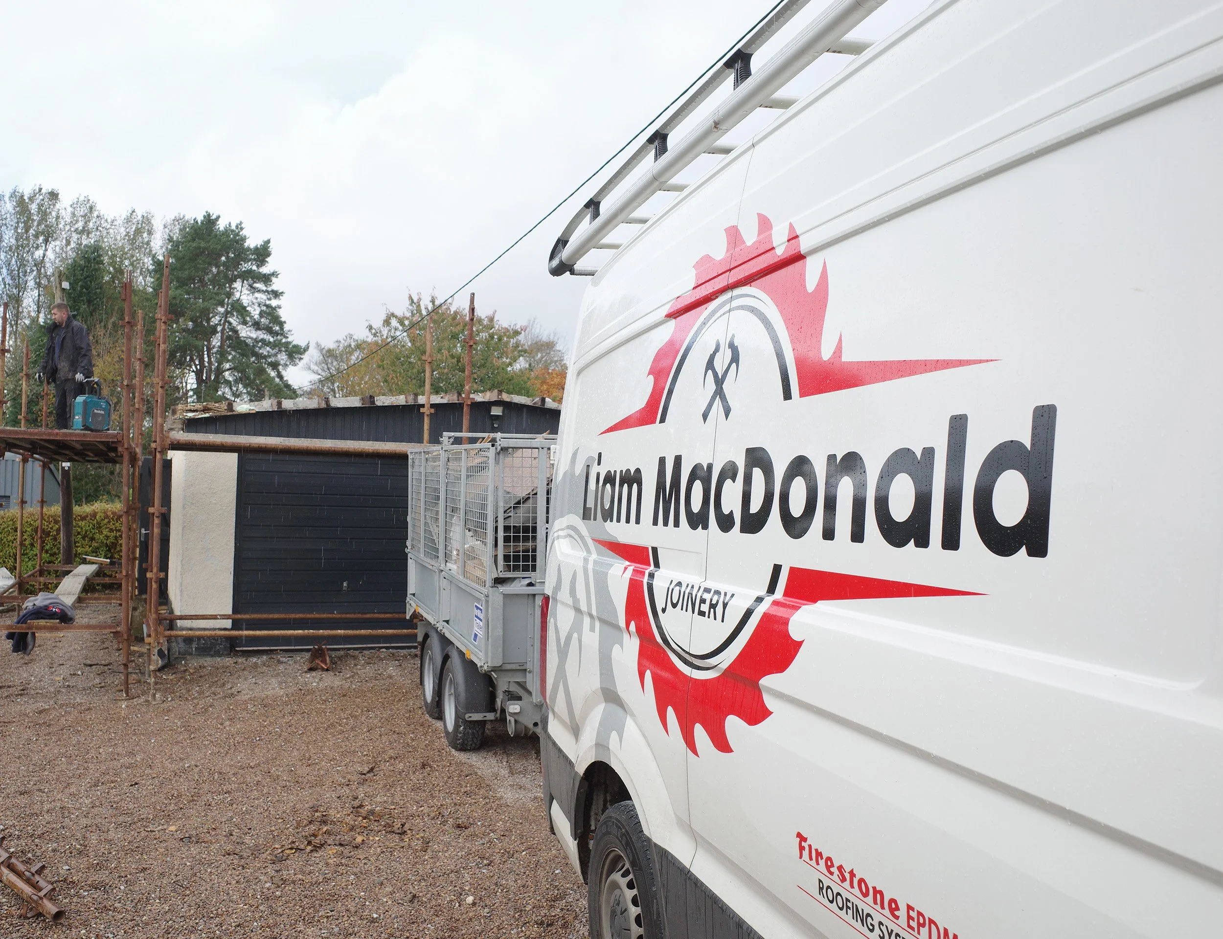 Construction worker standing on scaffolding next to a house under renovation, with a Liam MacDonald Joinery van in the foreground.