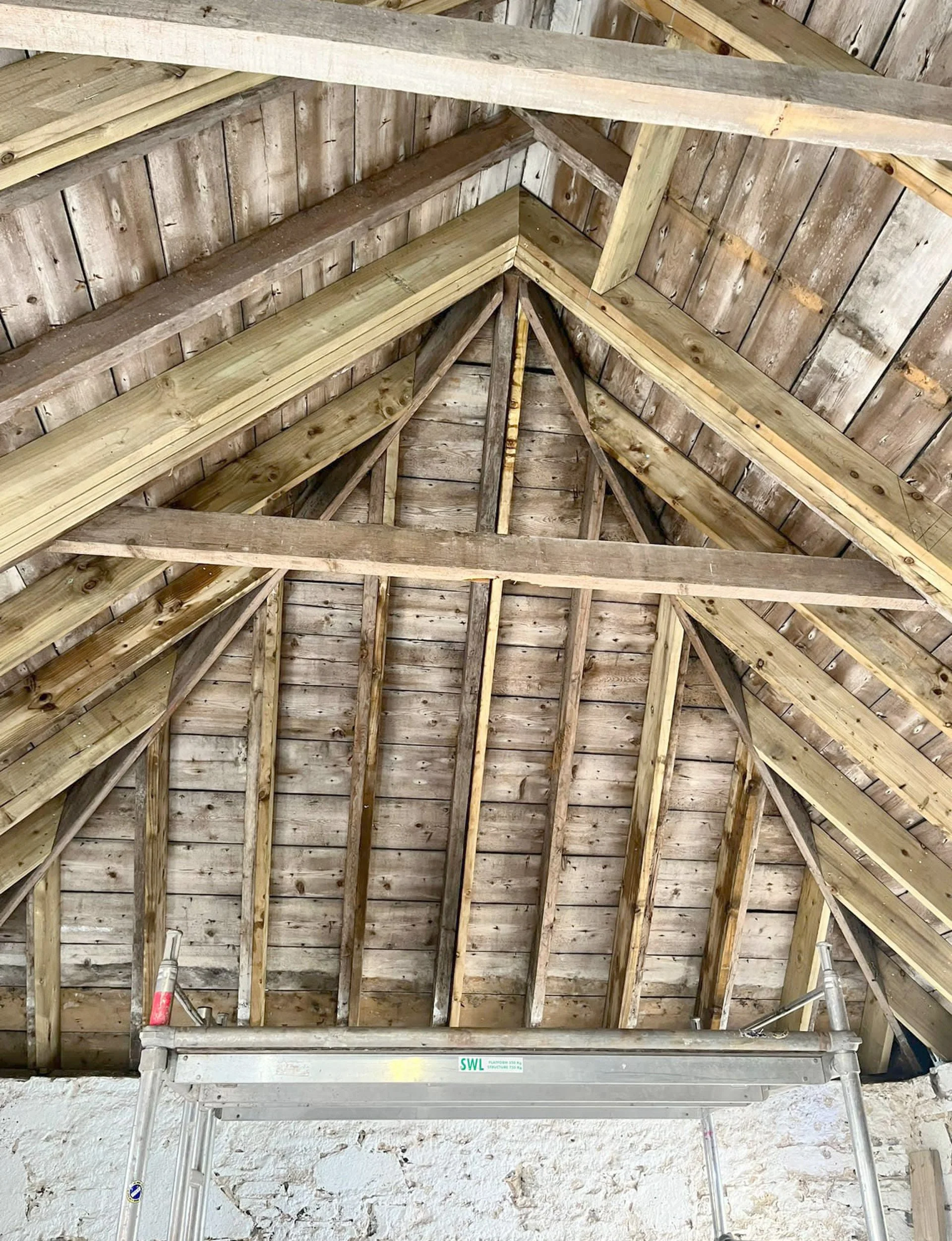 View of a wooden attic ceiling with exposed wooden beams and planks, and a ladder at the bottom.
