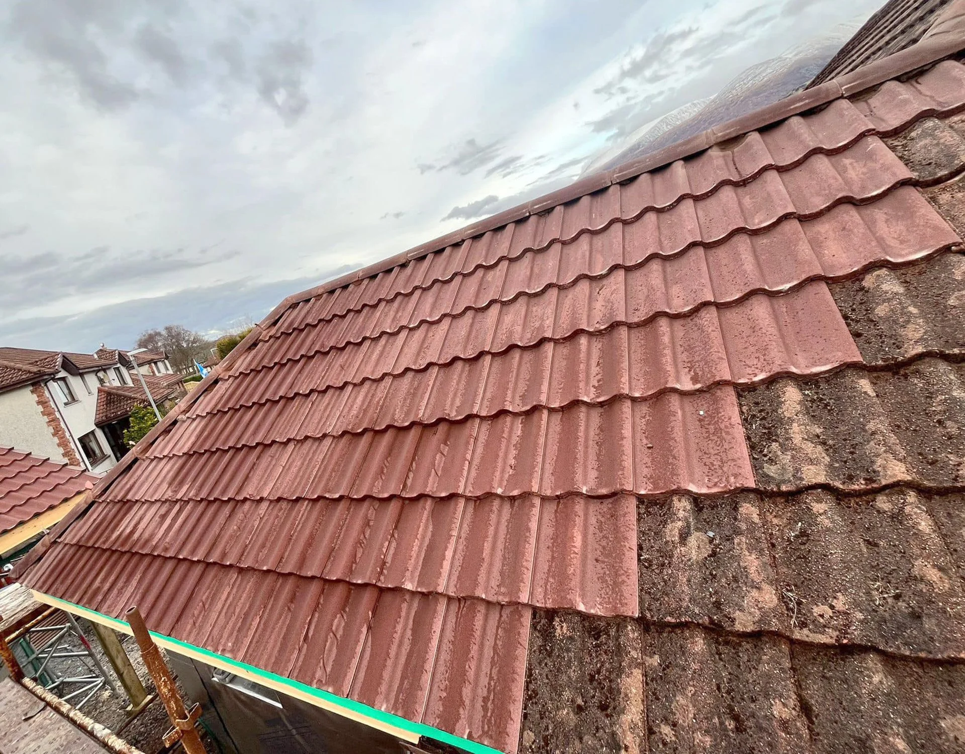 Close-up view of a roof with new red clay tiles and older weathered tiles on the right side during overcast weather.