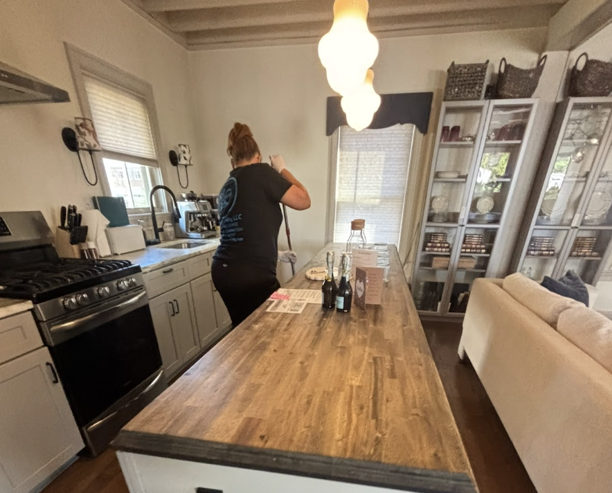 Woman preparing food in a cozy kitchen with a wooden island, gas stove, pendant lights, and glass-front cabinets.