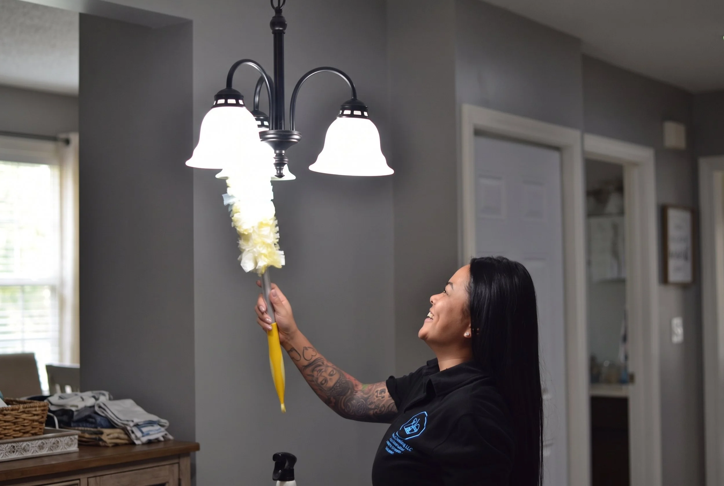 Woman cleaning a hanging three-light chandelier with a feather duster