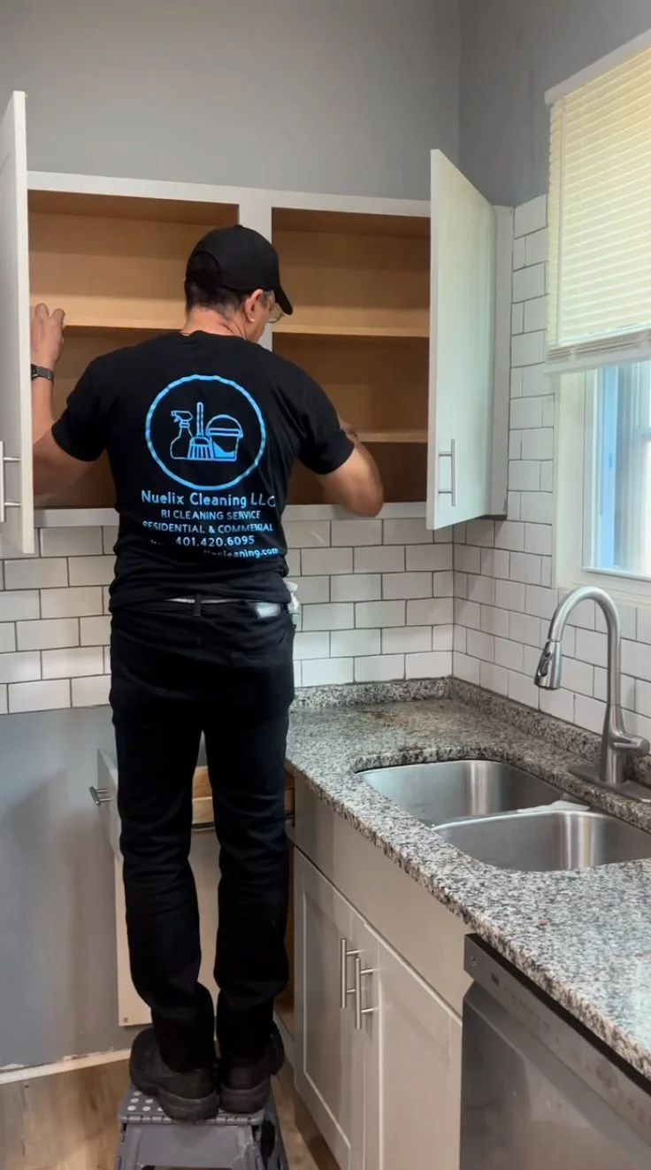 Professional cleaner organizing kitchen cabinets above a granite countertop and double sink
