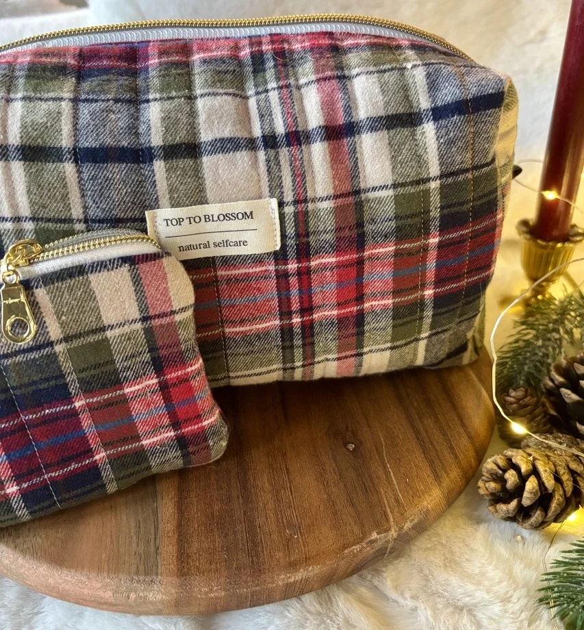 Een flanellen plaid getekende toilettas en een mini tas met dezelfde print, beide op een houten tafel naast kerstdecoraties.