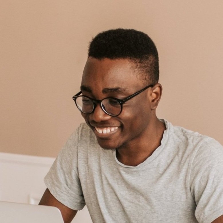 A smiling man with glasses looking at a laptop.