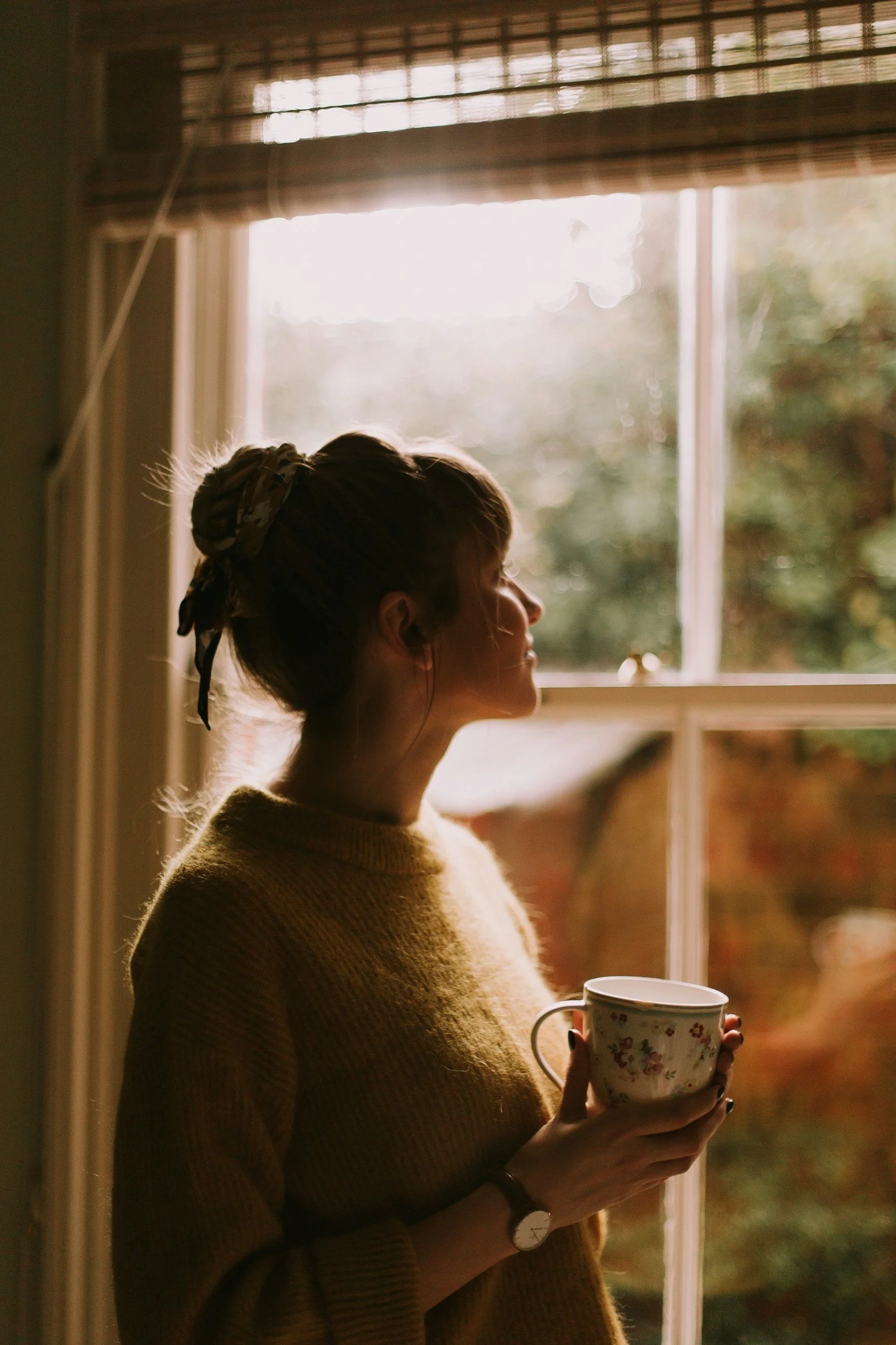 a new mom looks out a window with tea