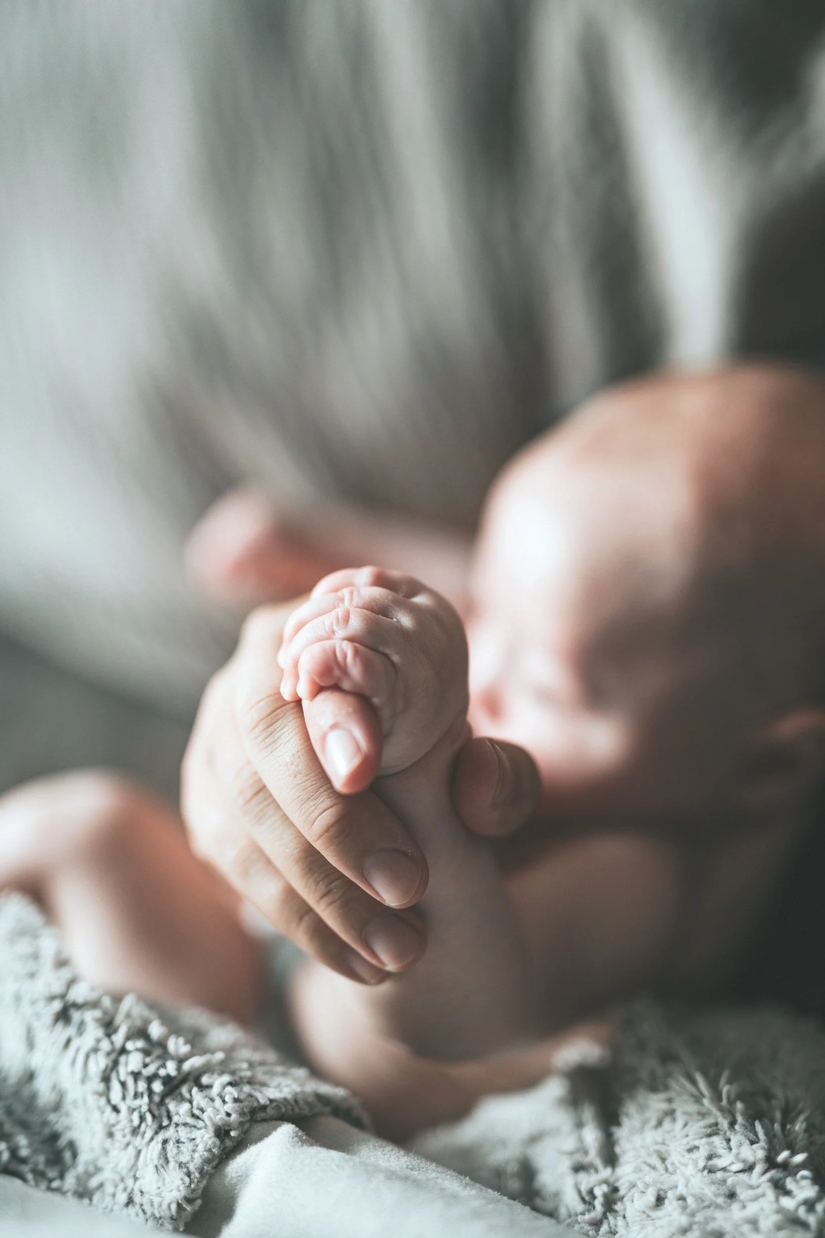 A mother holds a baby's palm on a blanket