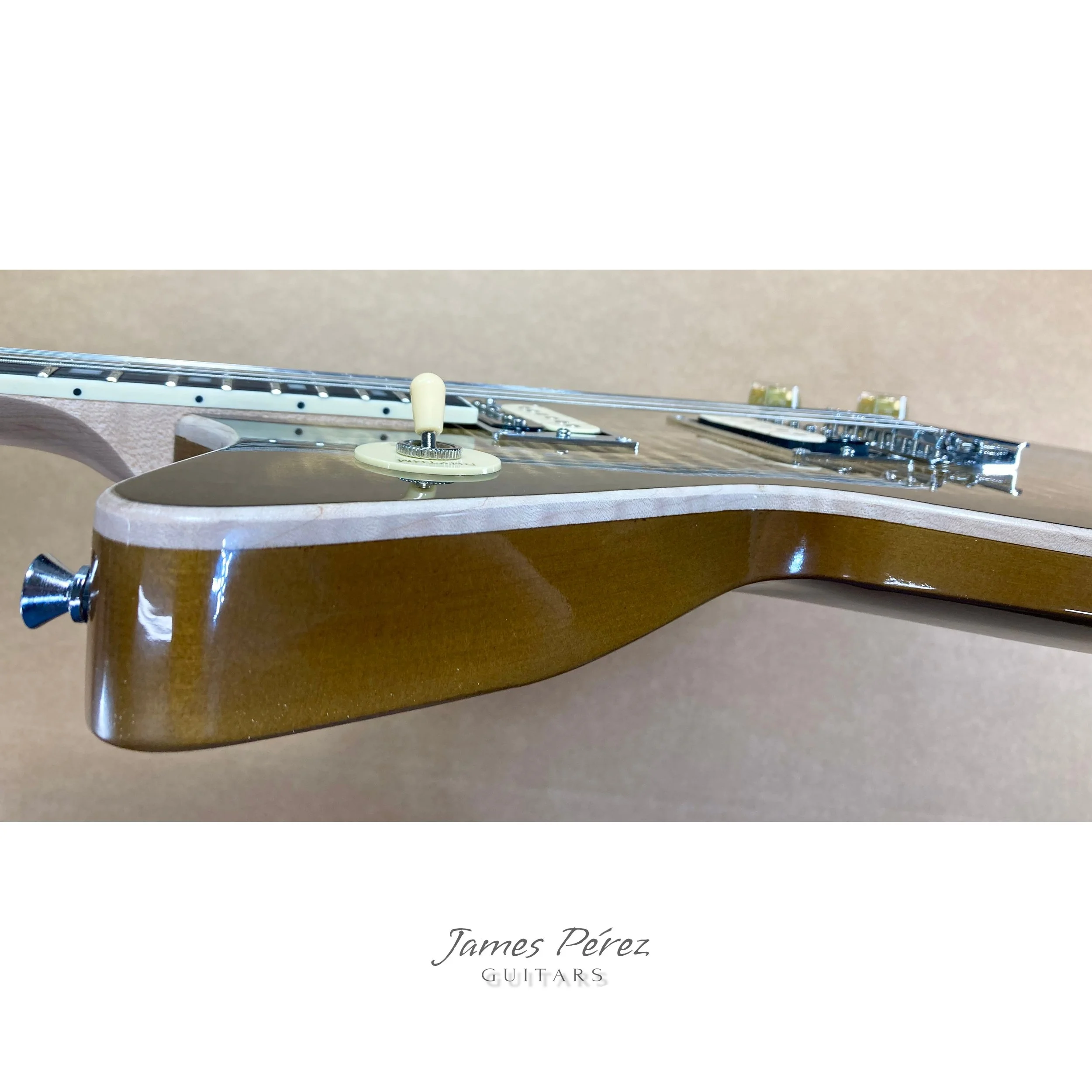 Close-up photograph of a brown electric guitar body, showing the neck, pickup, and control knobs, with the label 'James Pérez Guitars' at the bottom.