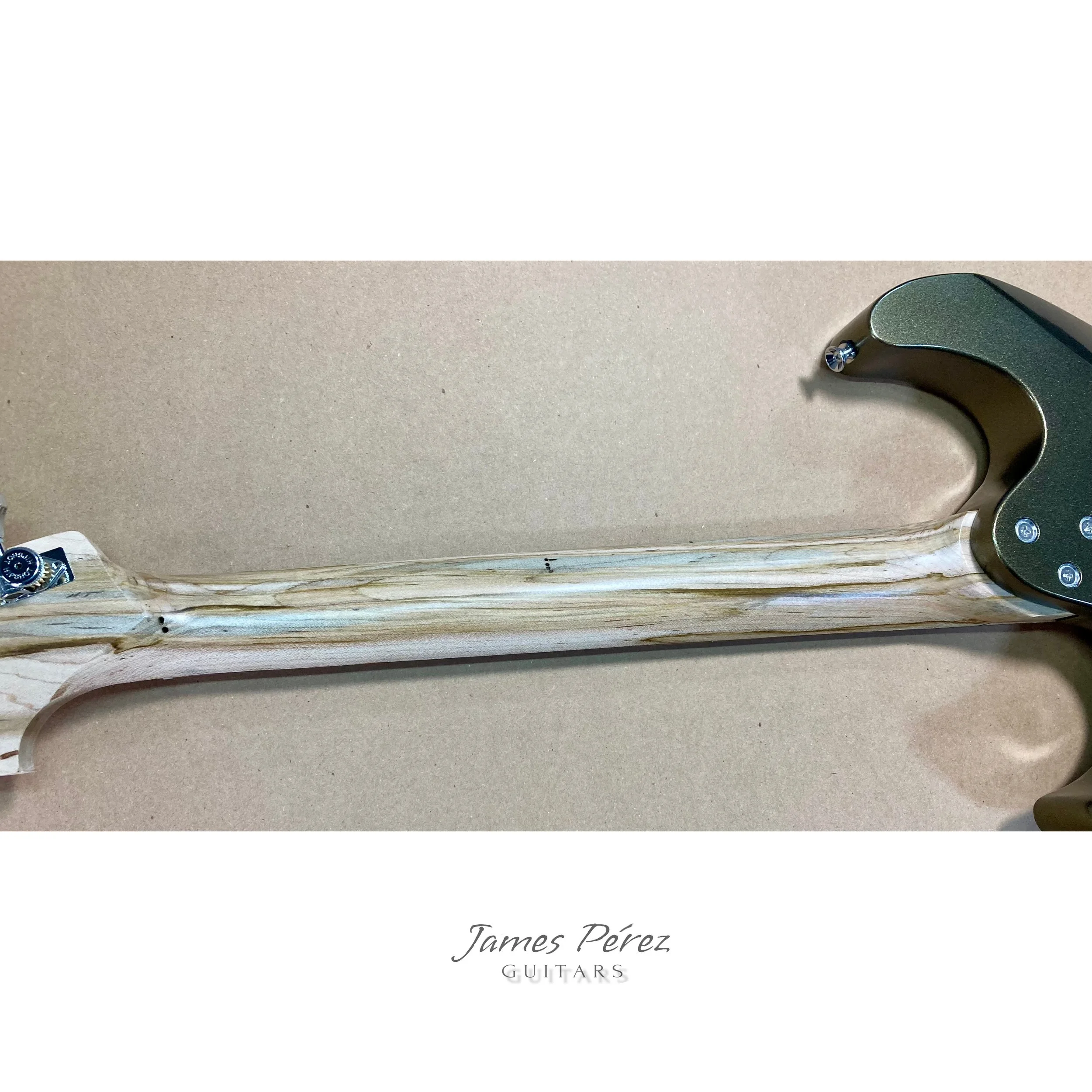 Close-up of the neck and headstock of an unfinished electric guitar guitar body with tuning pegs and bolts, placed on a beige surface, with text overlay reading 'James Pérez GUITARS'.