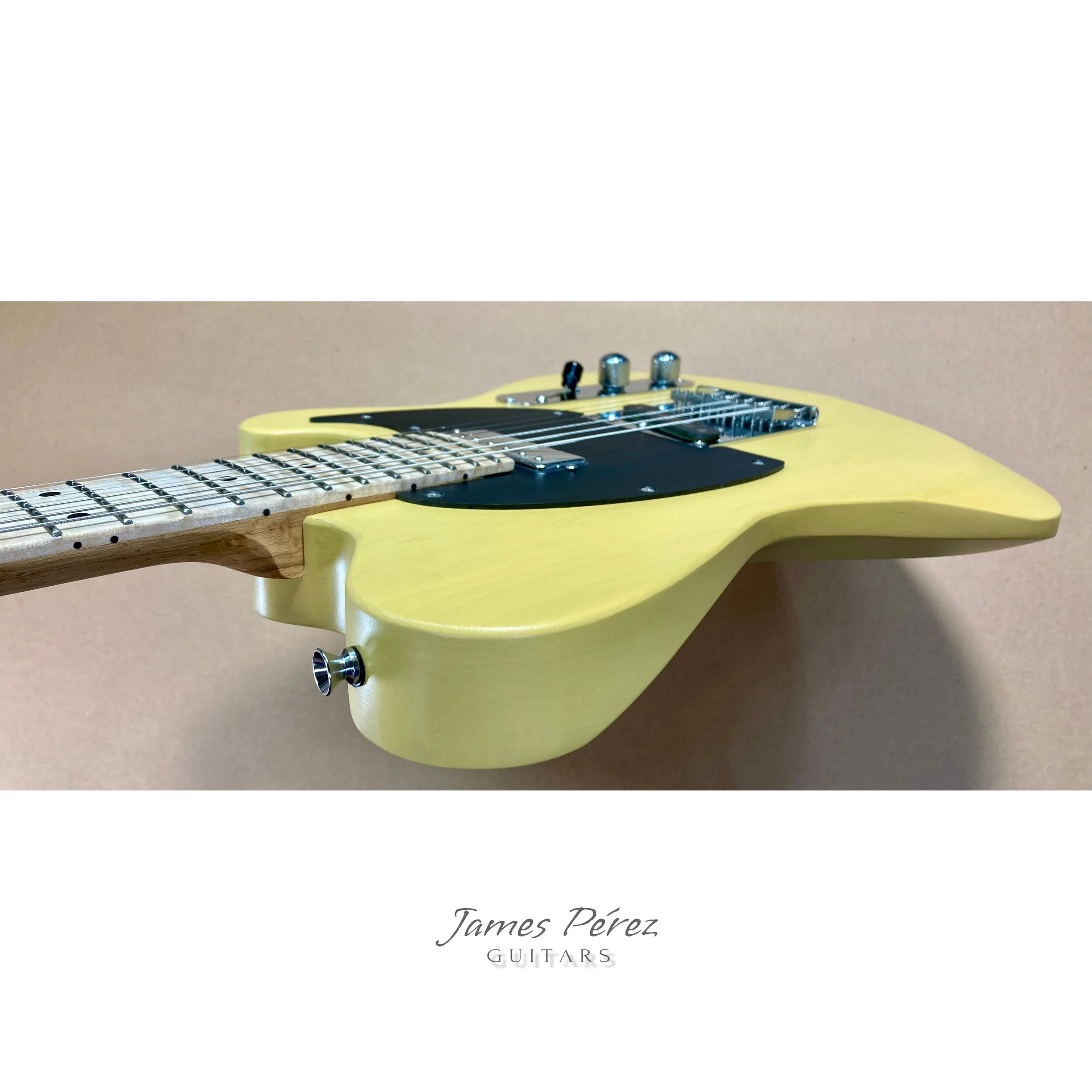 Yellow electric guitar with a black pickguard and a light wood neck, mounted on a light brown wall, withtext below reading 'James Pérez GUITARS'.