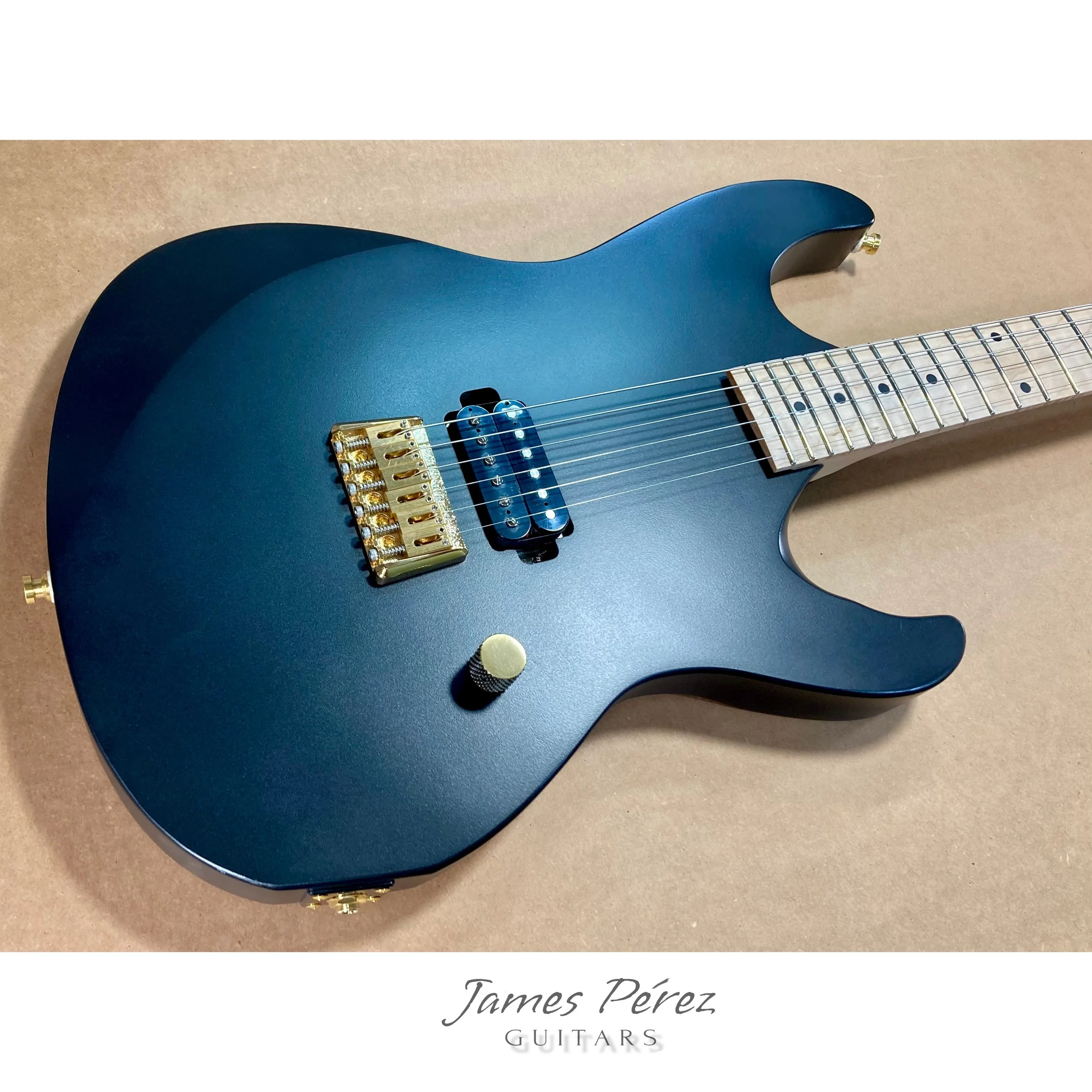 Black electric guitar with gold hardware, a single humbucker and single coil pickup, knob, and maple fretboard with dot inlays on a brown background with a white caption reading 'James Pérez GUITARS'.