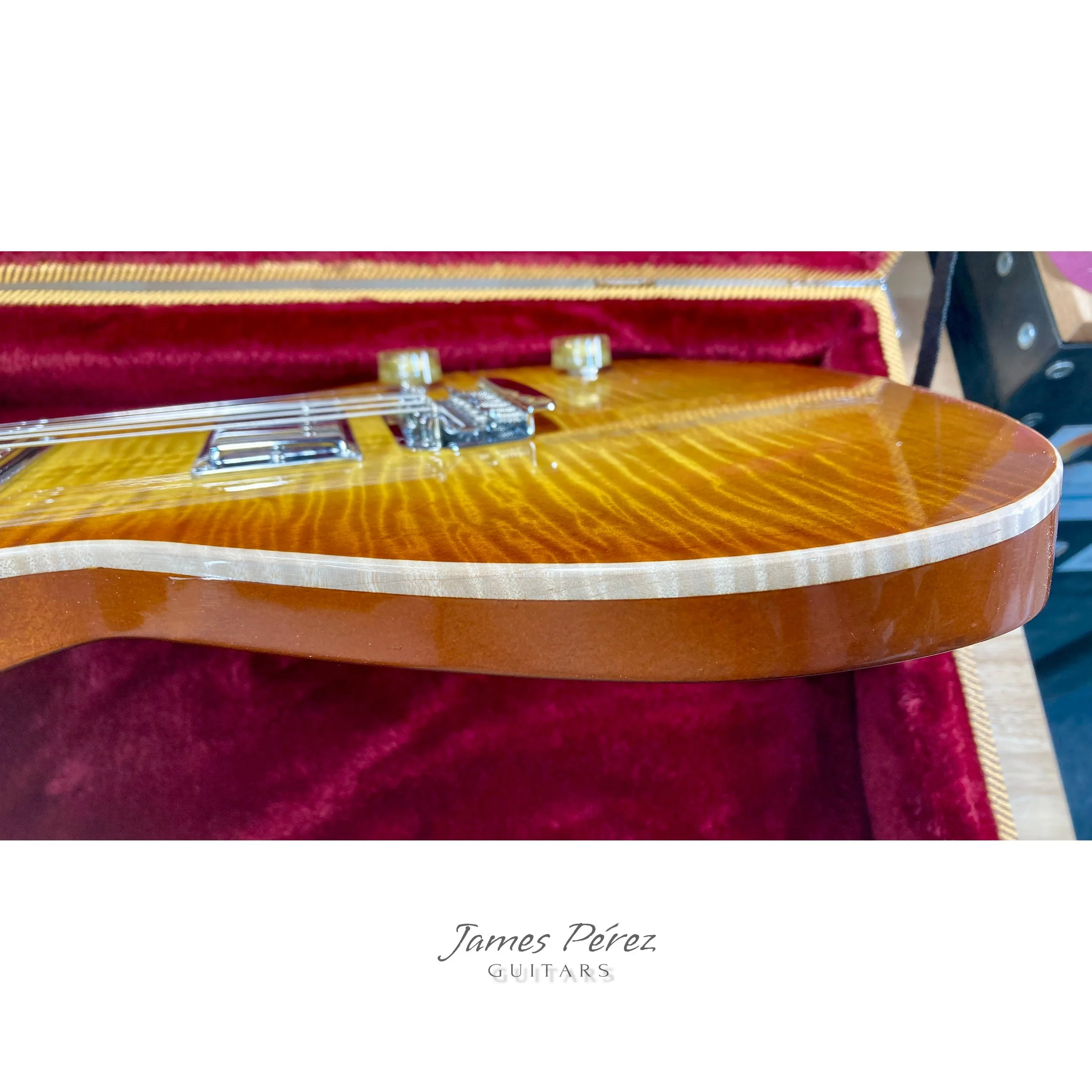 Close-up of a wooden electric guitar inside a red-lined case.