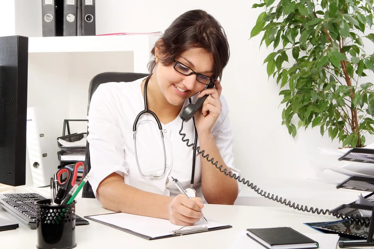 Profissional de saúde ao telefone na recepção da clínica, resolvendo manualmente o caso que uma IA de nível 2 encaminhou em vez de uma IA que resolve fechar