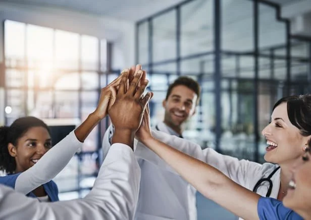 Equipe médica comemorando com toque de mãos, simbolizando bons resultados de satisfação do paciente em clínicas