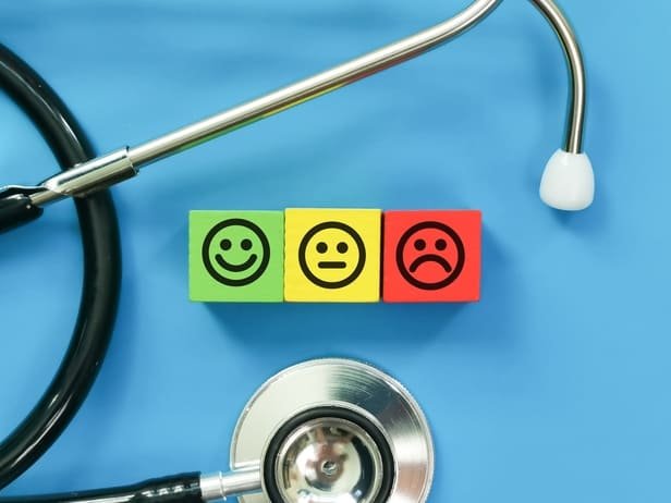Blocos com emojis feliz, neutro e triste ao lado de estetoscópio, representando a escala de CSAT em clínicas