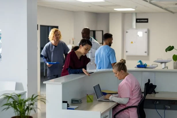 Recepção de clínica sobrecarregada com equipe atendendo vários pacientes ao mesmo tempo