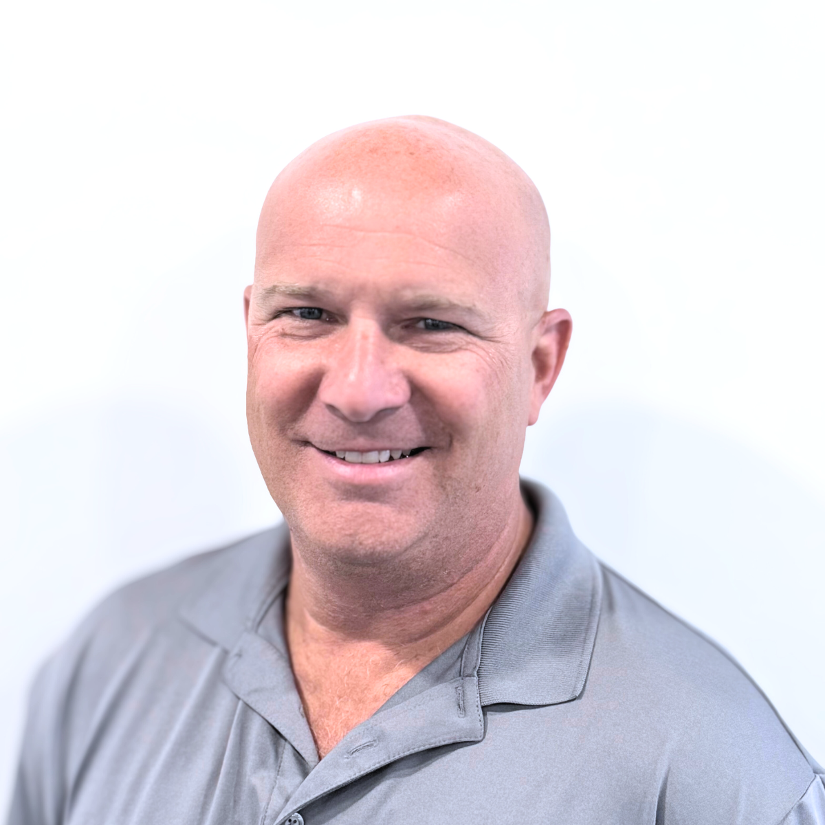 Close-up portrait of a smiling bald man wearing a gray polo shirt against a plain white background.