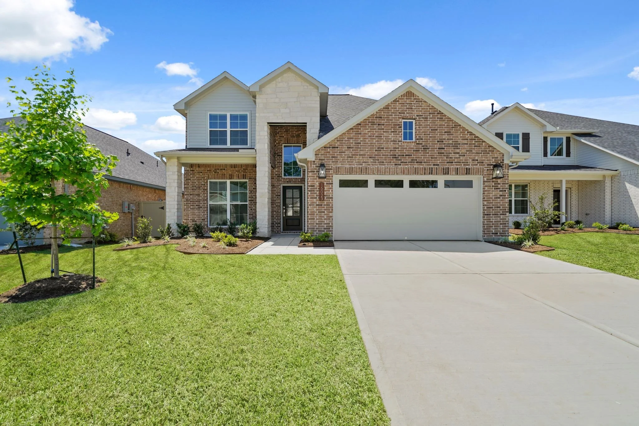 A modern two-story house with a brick and white siding exterior, a garage, and a well-maintained lawn under a blue sky.