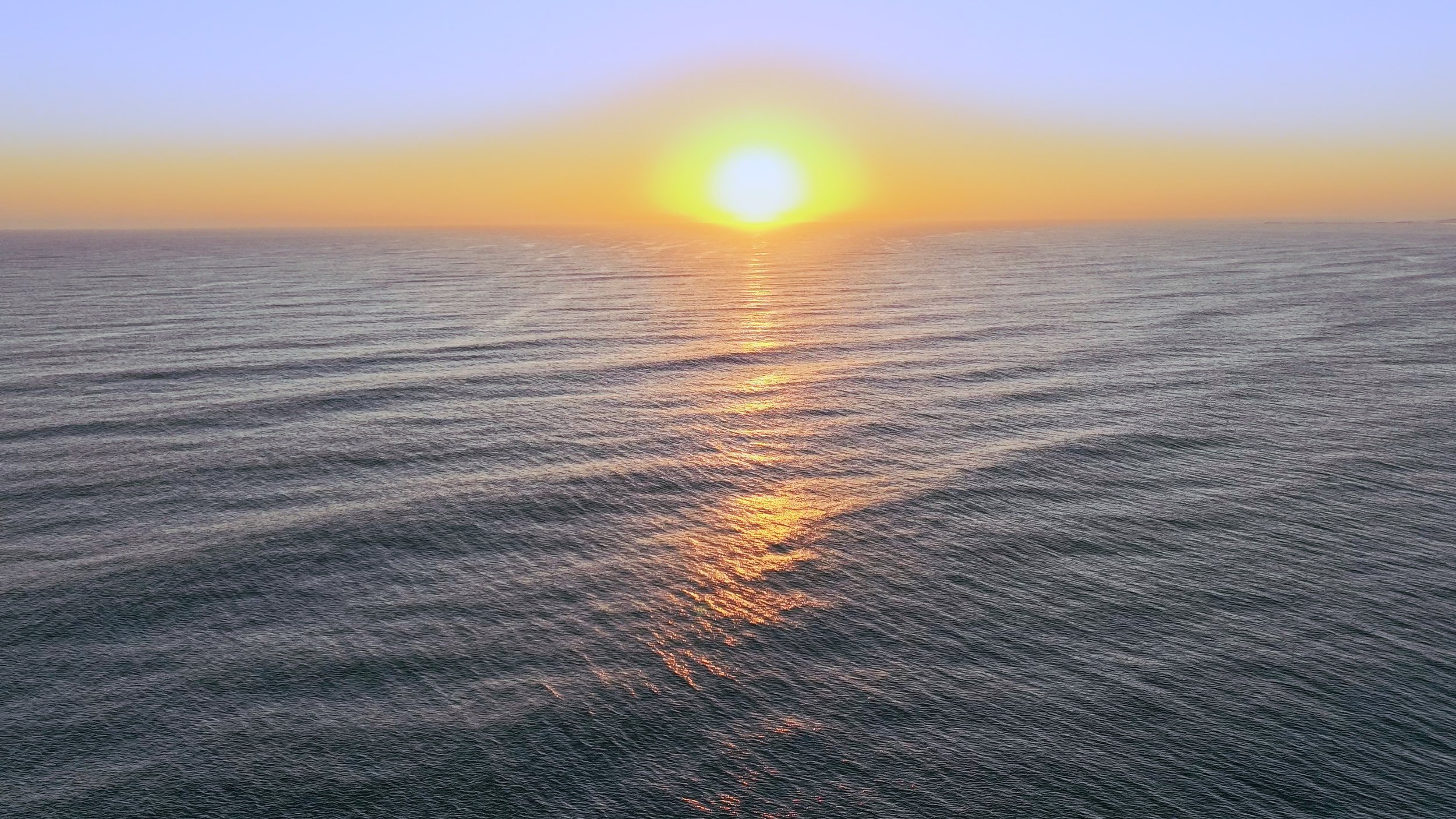 Sunset over the ocean with gentle waves and a reflection of the sun on the water.