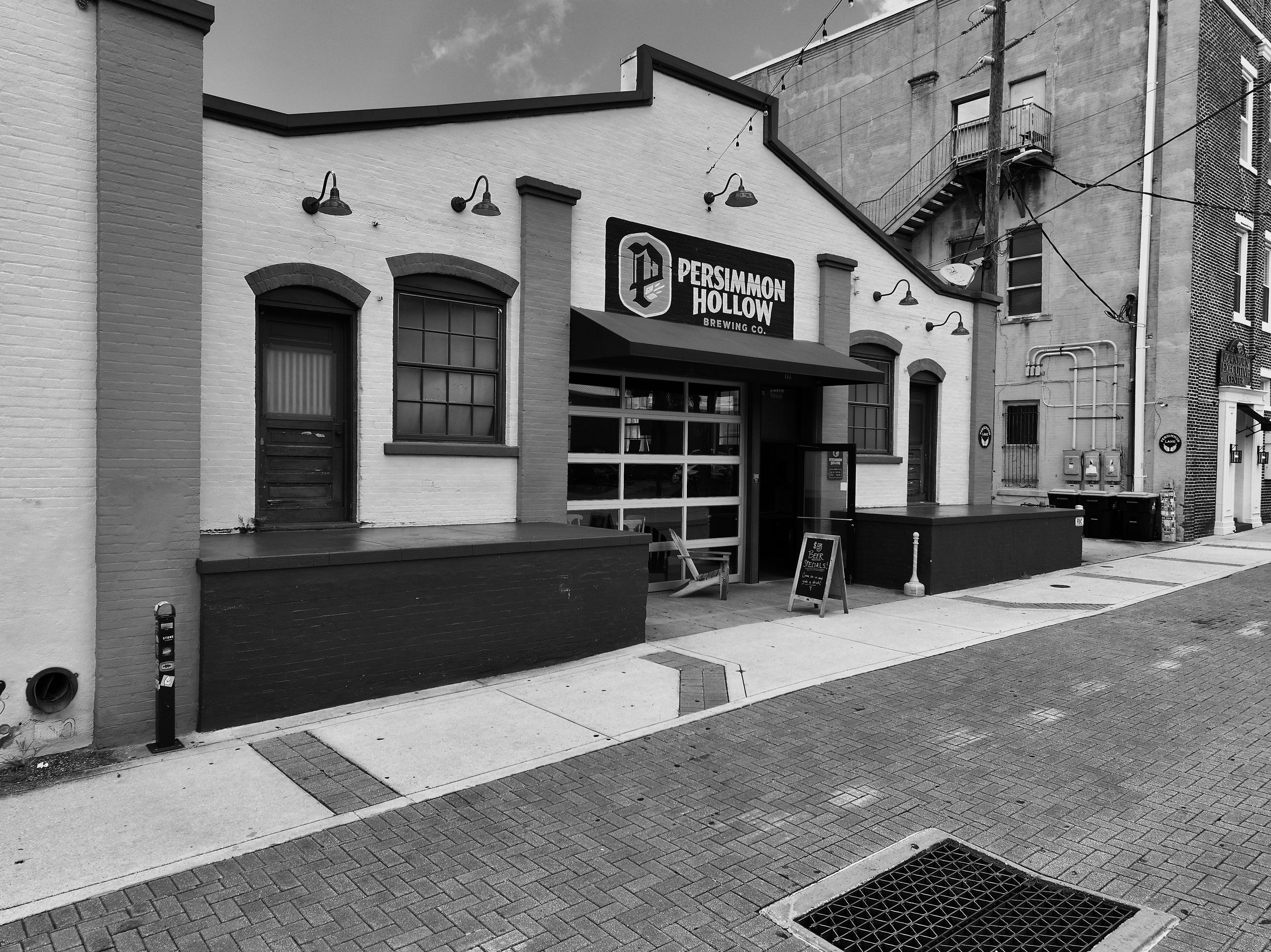 Exterior view of Persimmon Hollow Brewing Co. Brick road and neighboring buildings are visible. Artisan Alley, DeLand, Florida. DJI Mavic 3 Pro. Professional drone photography.  Volusia County.