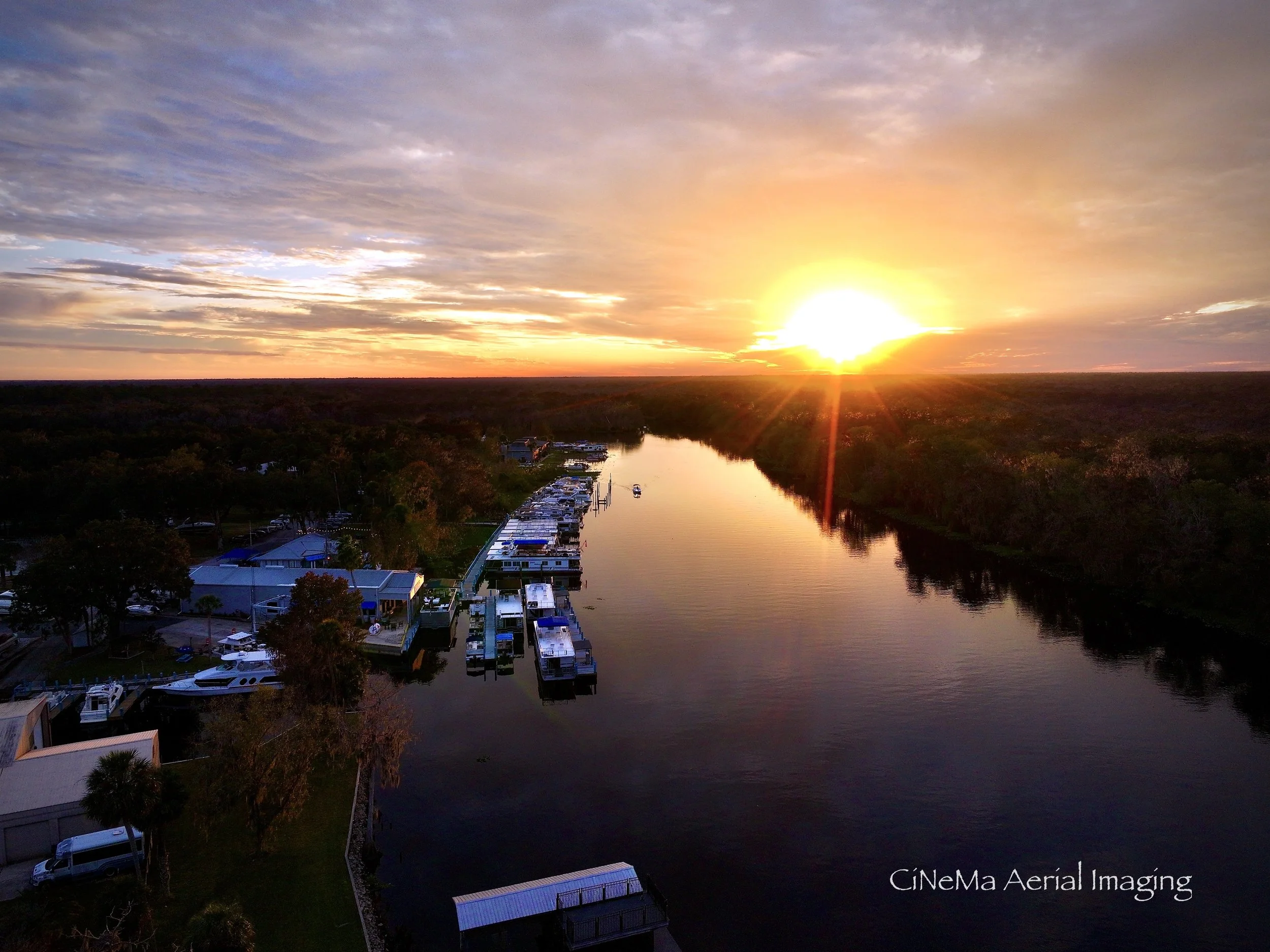 Aerial view of a lush green landscape with water bodies, boats, and buildings during sunset with a colorful sky. Holly Bluff Marina in DeLand, Florida. Drone photography and videography. Professional aerial data capture services.