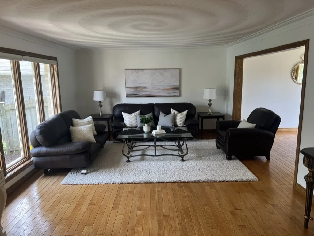 Living room with three black leather sofas, a glass coffee table, a white rug, two table lamps, and a painting on the wall.