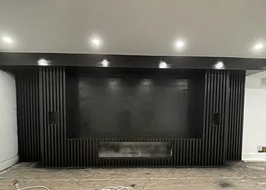 Modern black entertainment wall with a large flat-screen TV, flanked by black vertical slats and a metallic fireplace below.