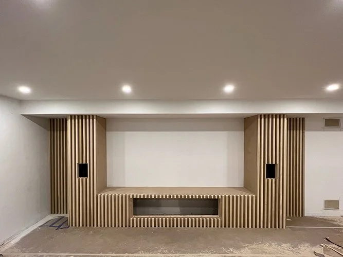 Interior view of a room with wood paneling and two black speakers on either side, with a blank white wall in the center.