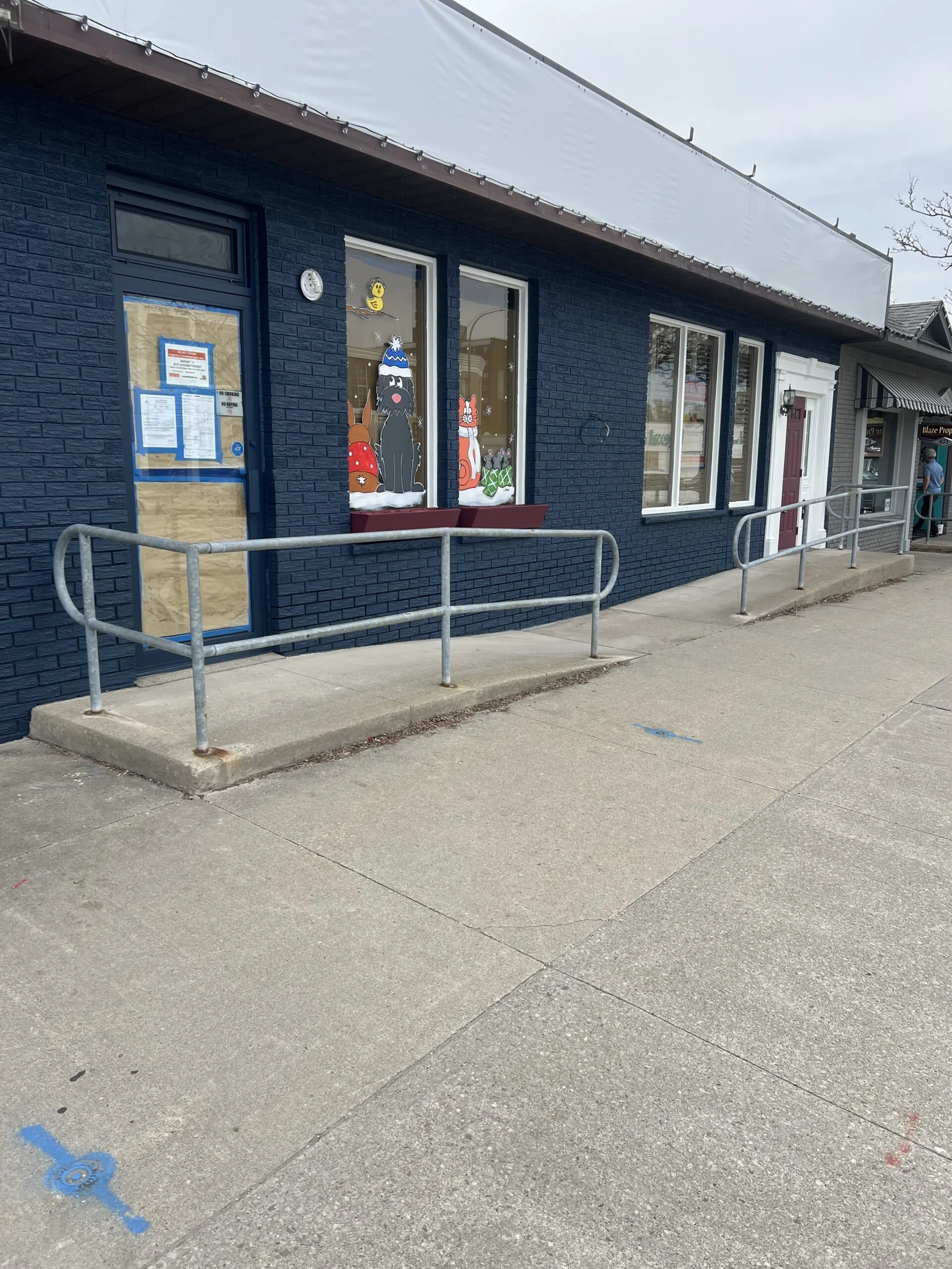 A storefront painted in dark blue with holiday-themed window decorations featuring cartoon-style animals and gifts.