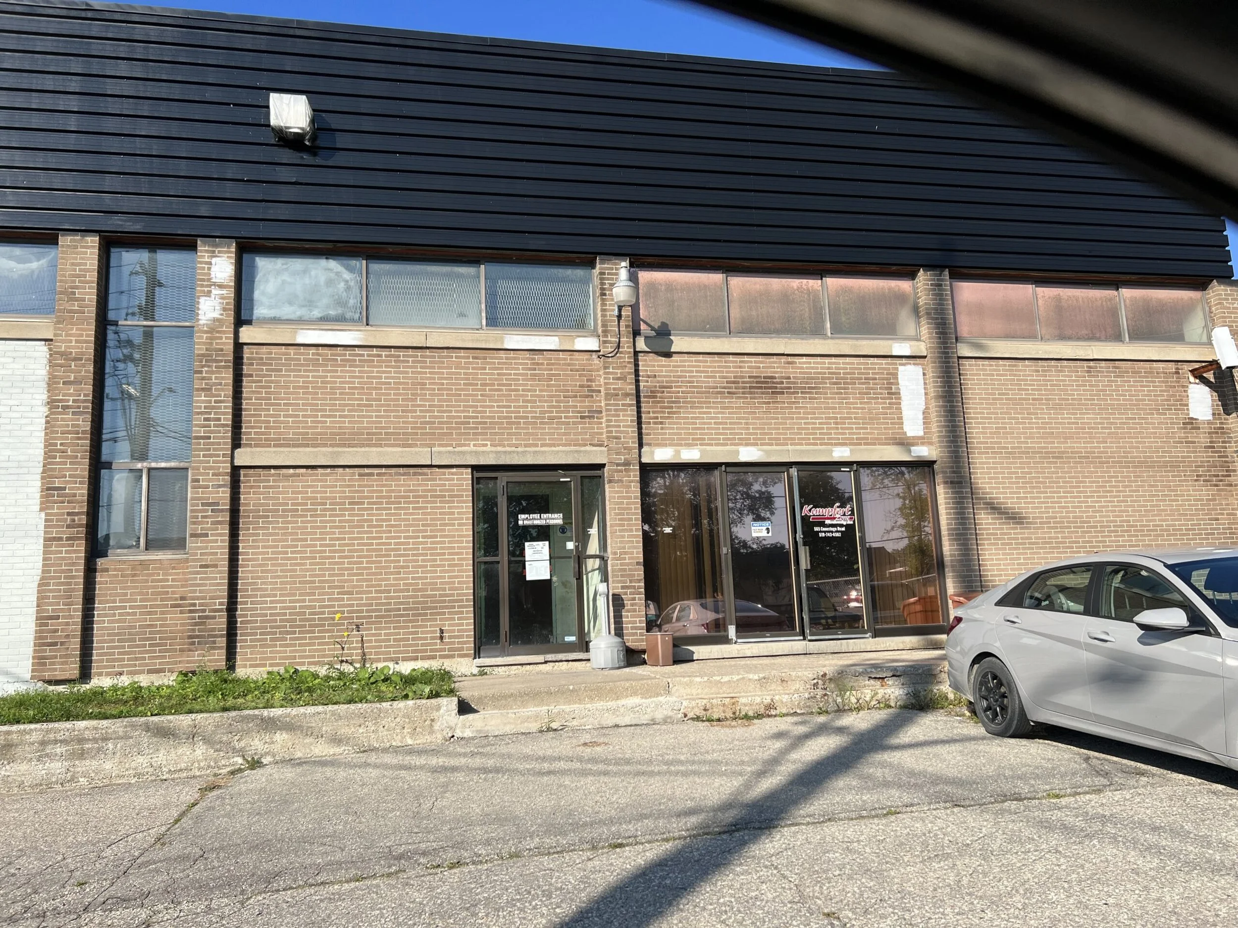 Exterior view of a brick commercial building with large windows and a glass door, with a silver car parked in front.
