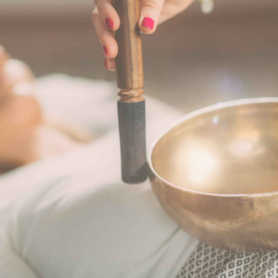 Person holding a mallet above a singing bowl, preparing to strike it.