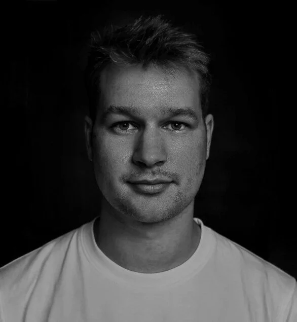 Black and white portrait of a young man with short hair, wearing a white T-shirt, looking at the camera with a slight smile.