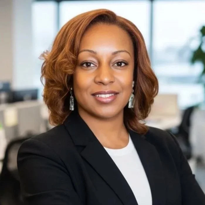 Professional woman with shoulder-length reddish-brown hair in an office setting wearing a black blazer and earrings, smiling confidently. Livewire Government Solutions