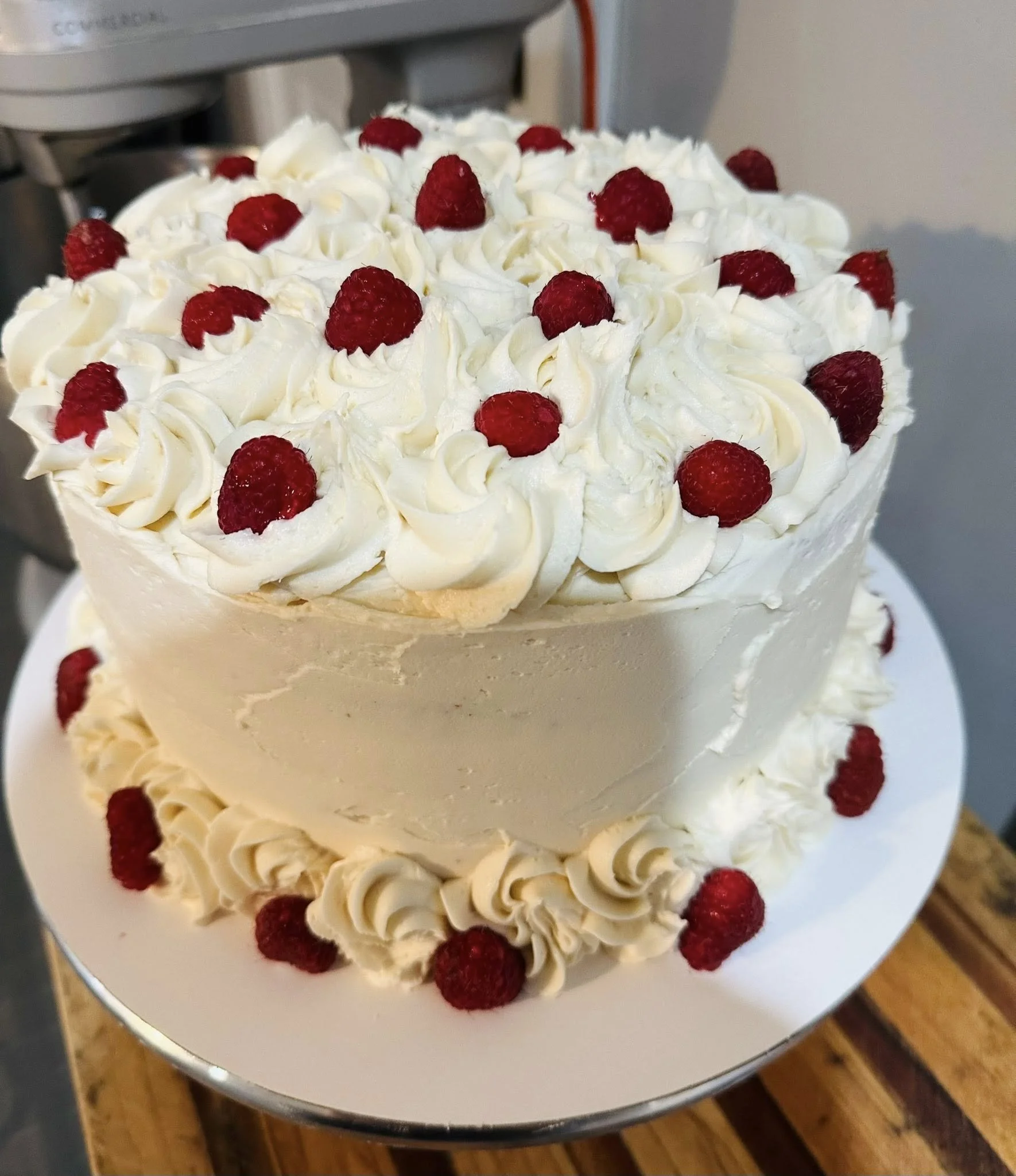 A two-tiered white cake decorated with swirls of white frosting and topped with raspberries.