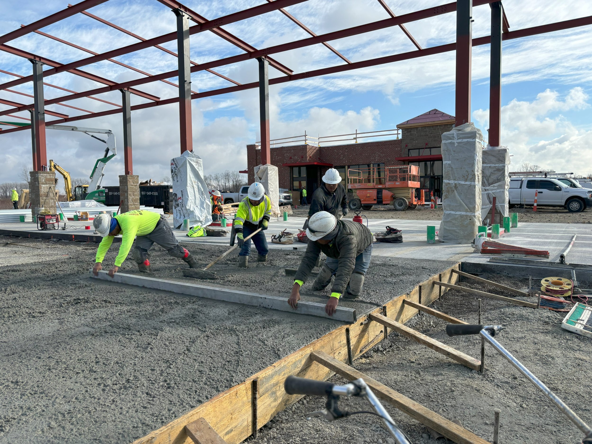 Construction workers in hard hats and reflective vests working on pouring and smoothing concrete for building foundation or floor at a construction site.
