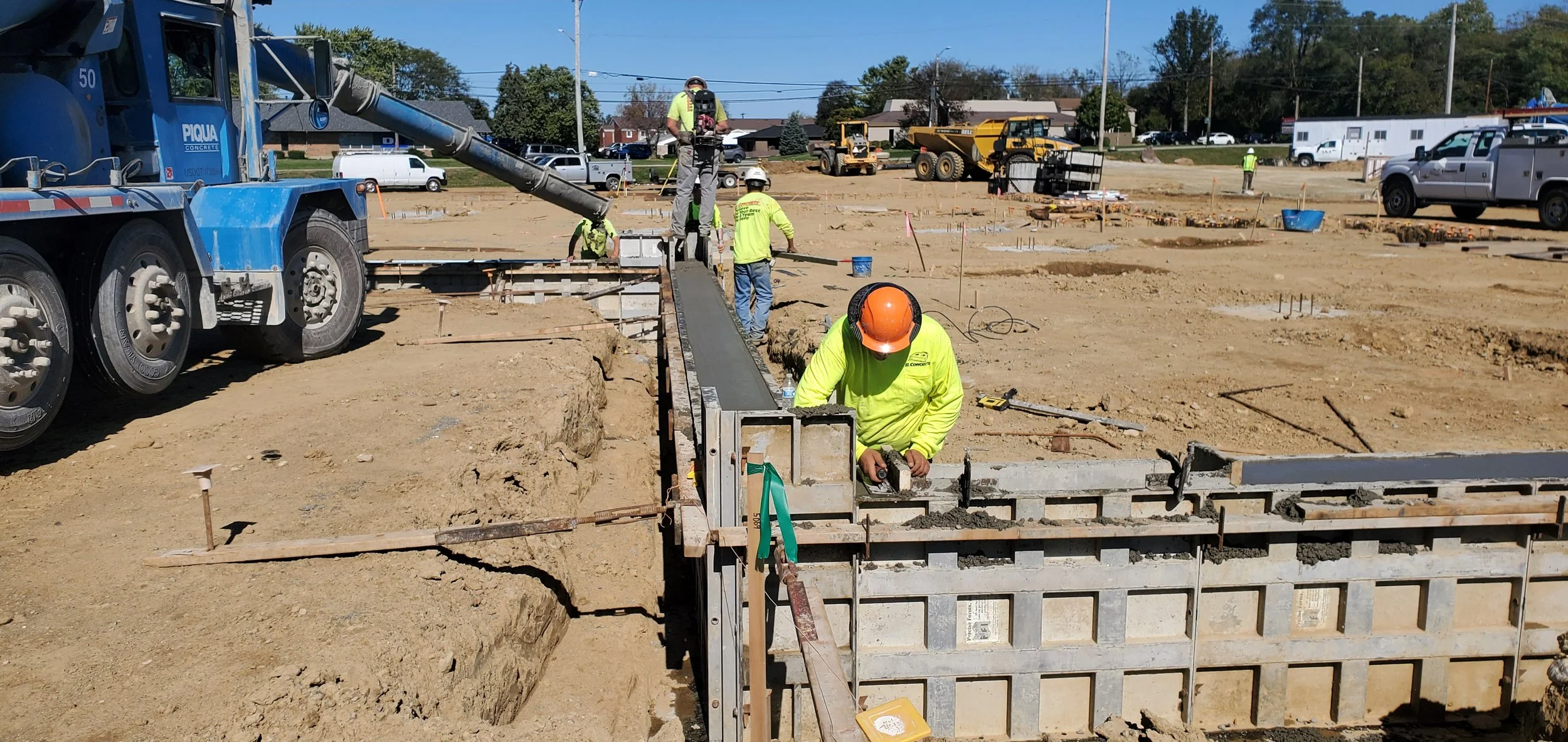 Construction workers in safety gear working on concrete formwork at a construction site with industrial vehicles and equipment in the background.