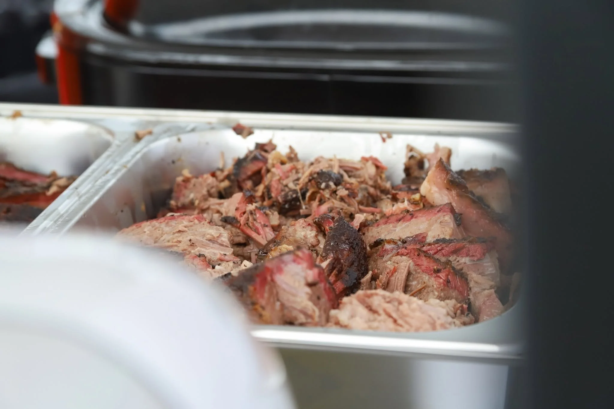 Close-up of shredded or pulled cooked meat inside a metal tray, with a blurred background showing a stove or oven.