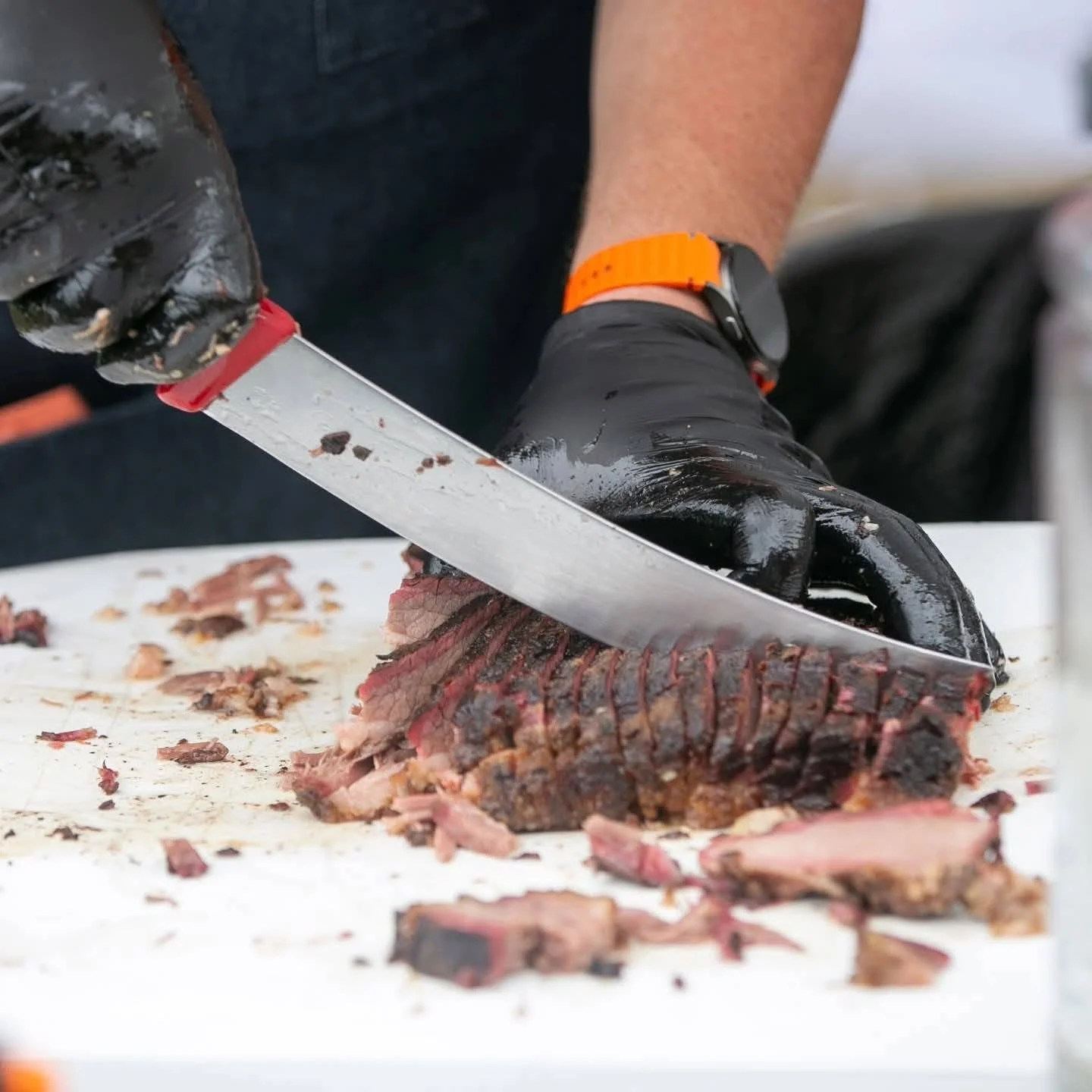 Person slicing smoked brisket with a large knife on a cutting board.