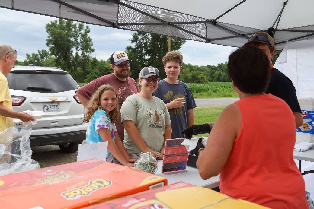 People ordered food at a food stand outdoors with a tent, a family standing in line and smiling.