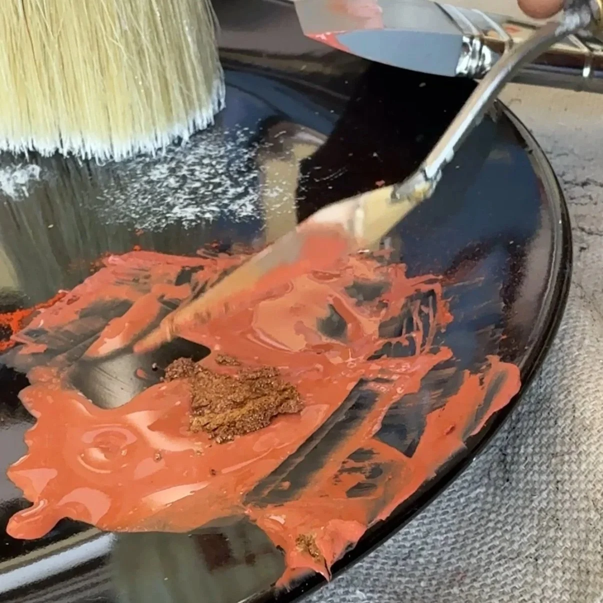 A close-up of a paint resurfacing machine in use, with orange paint and brown debris on the black circular surface.