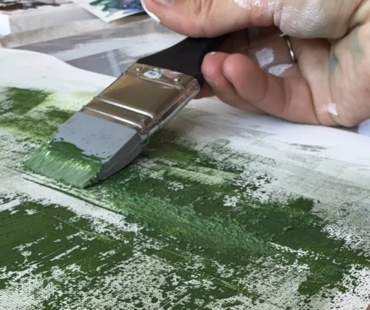Person using a foam roller to create an abstract painting with green and white paint on paper.