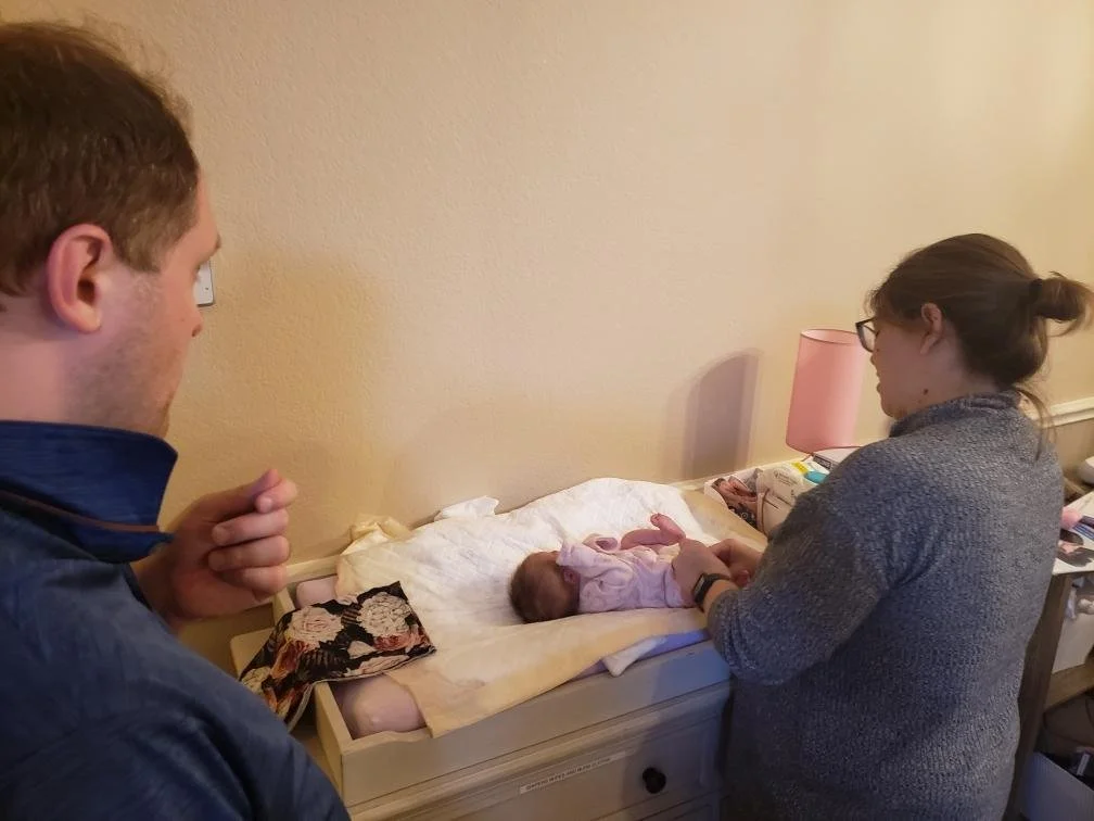 Doula Melanie Powell showing a new dad how to change a diaper as a part of postpartum doula services offered in person in Dallas Fort Worth Texas