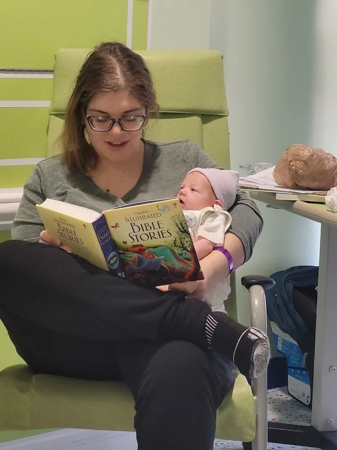 "Postpartum mom reading to her new baby in the hospital."