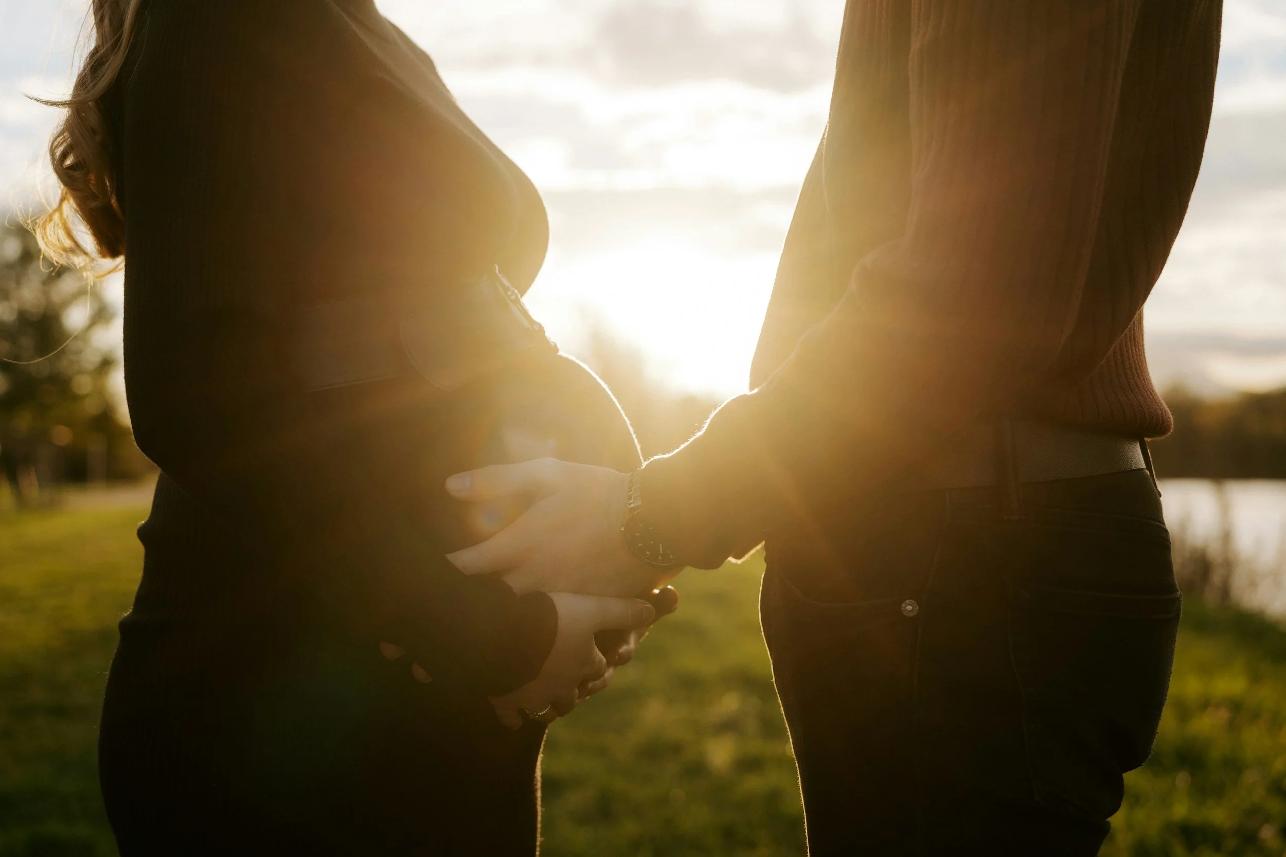 "Dad holding mom's pregnant belly with the sun shinning between them"