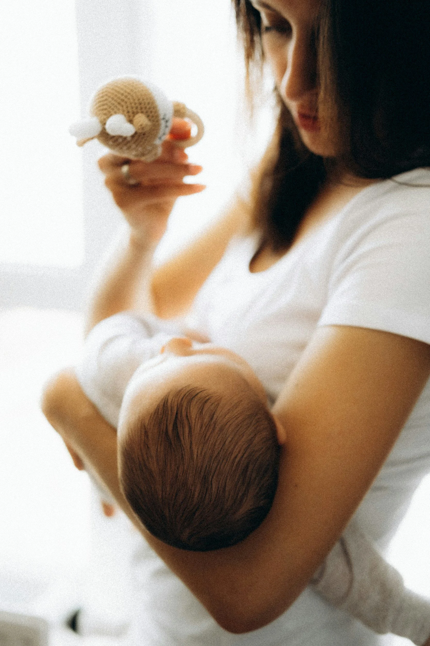 "New mom holding a toy as she breastfeeds her baby"