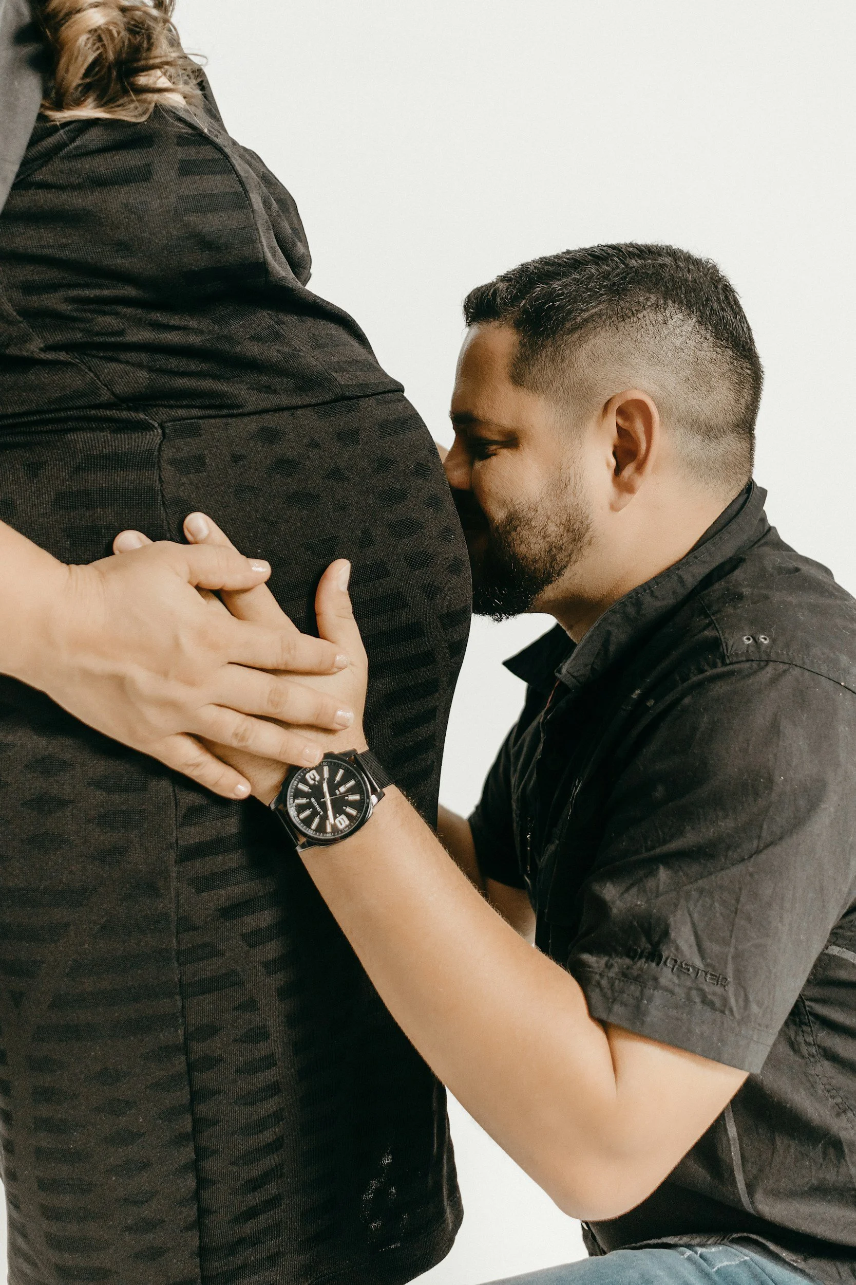 "Dad kneeling next to pregnant mom kissing her belly"