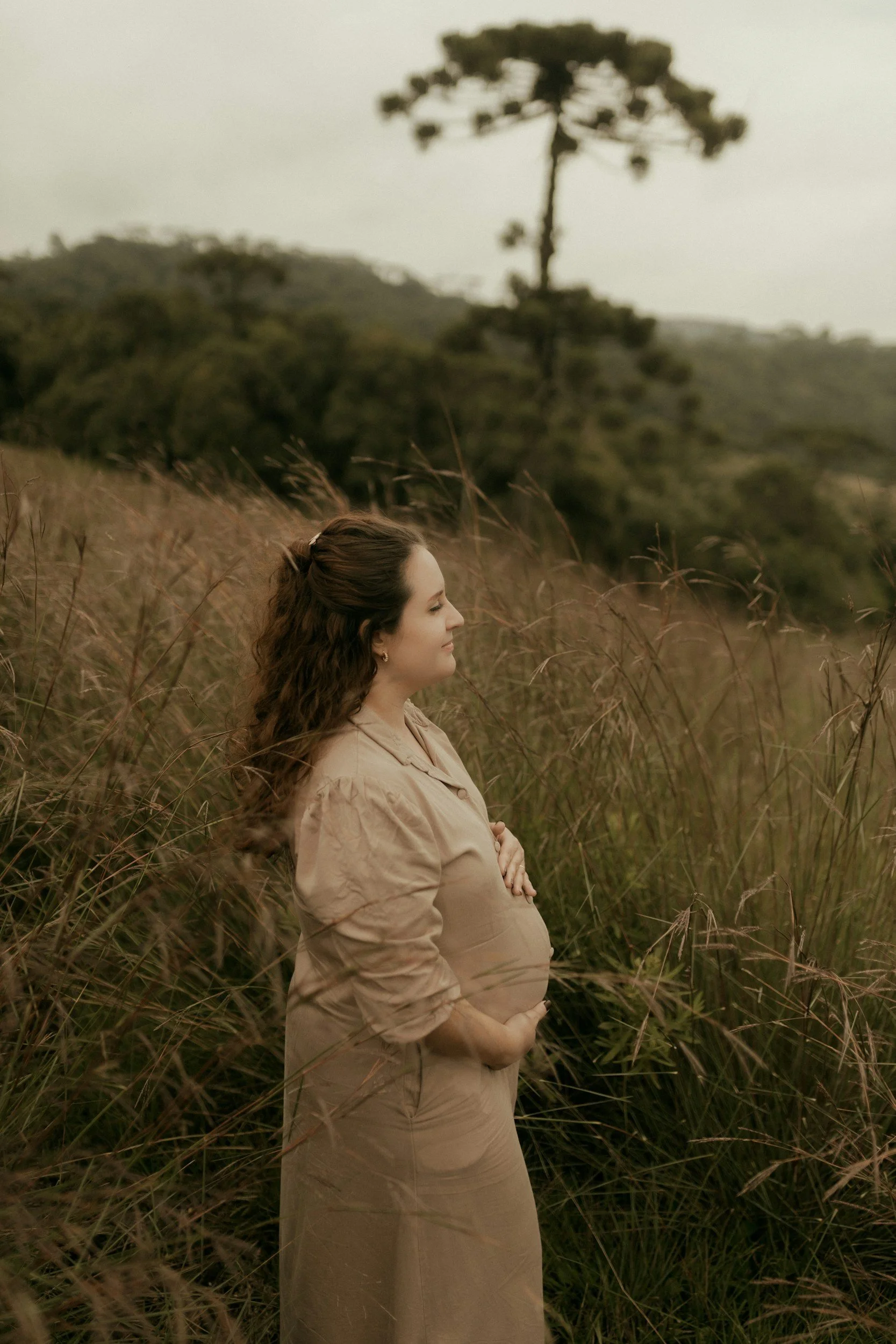 Pregnant mom standing in a field relaxed hugging her belly