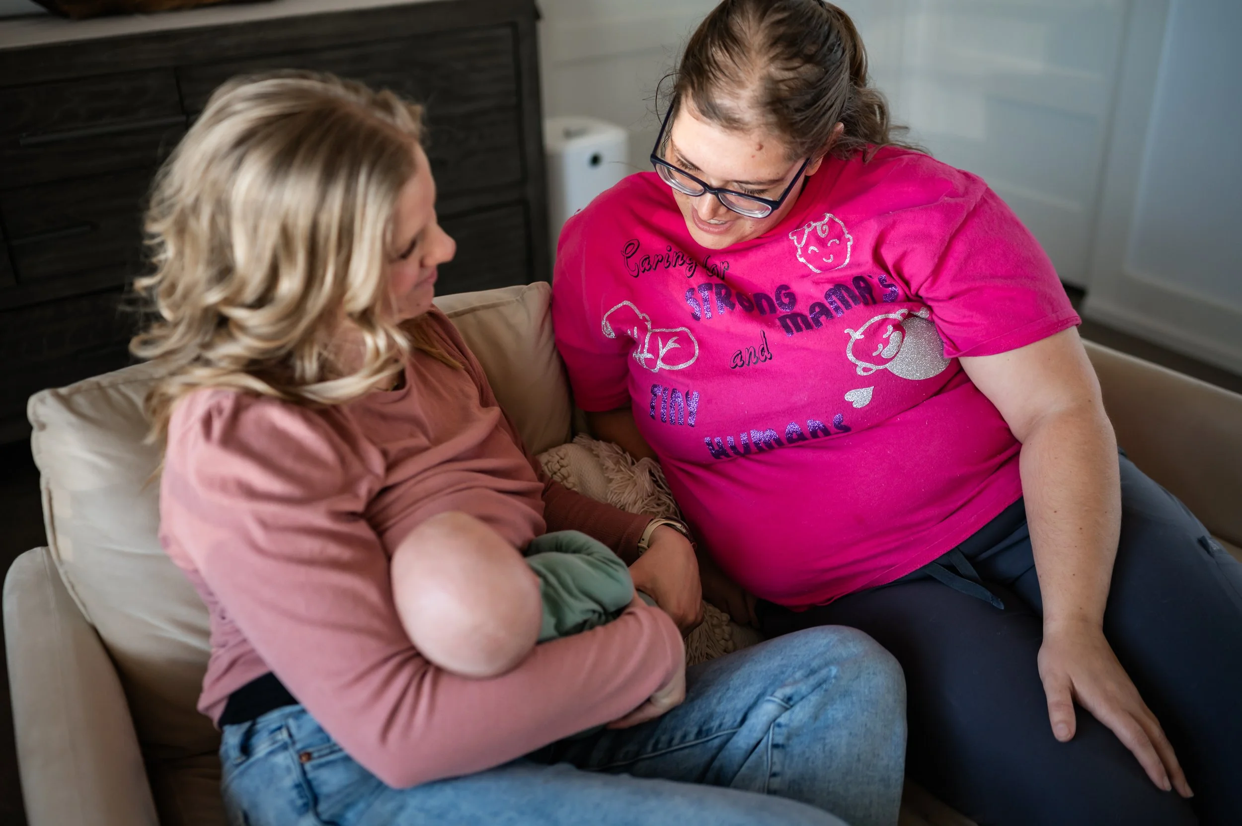 Doula Melanie Powell sitting next to a nursing mother looking down and smiling.