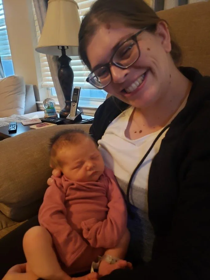 "Doula Melanie Powell smiling holding a peacefully sleeping newborn while relaxing together."