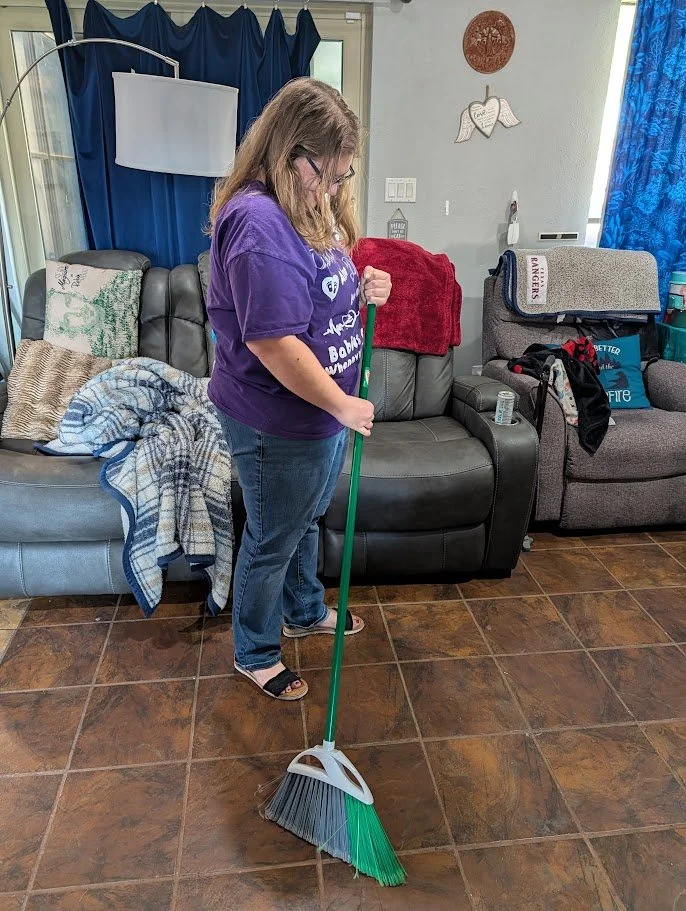 Doula Melanie Powell offering light housekeeping by sweeping clients living room in a Mansfield home.