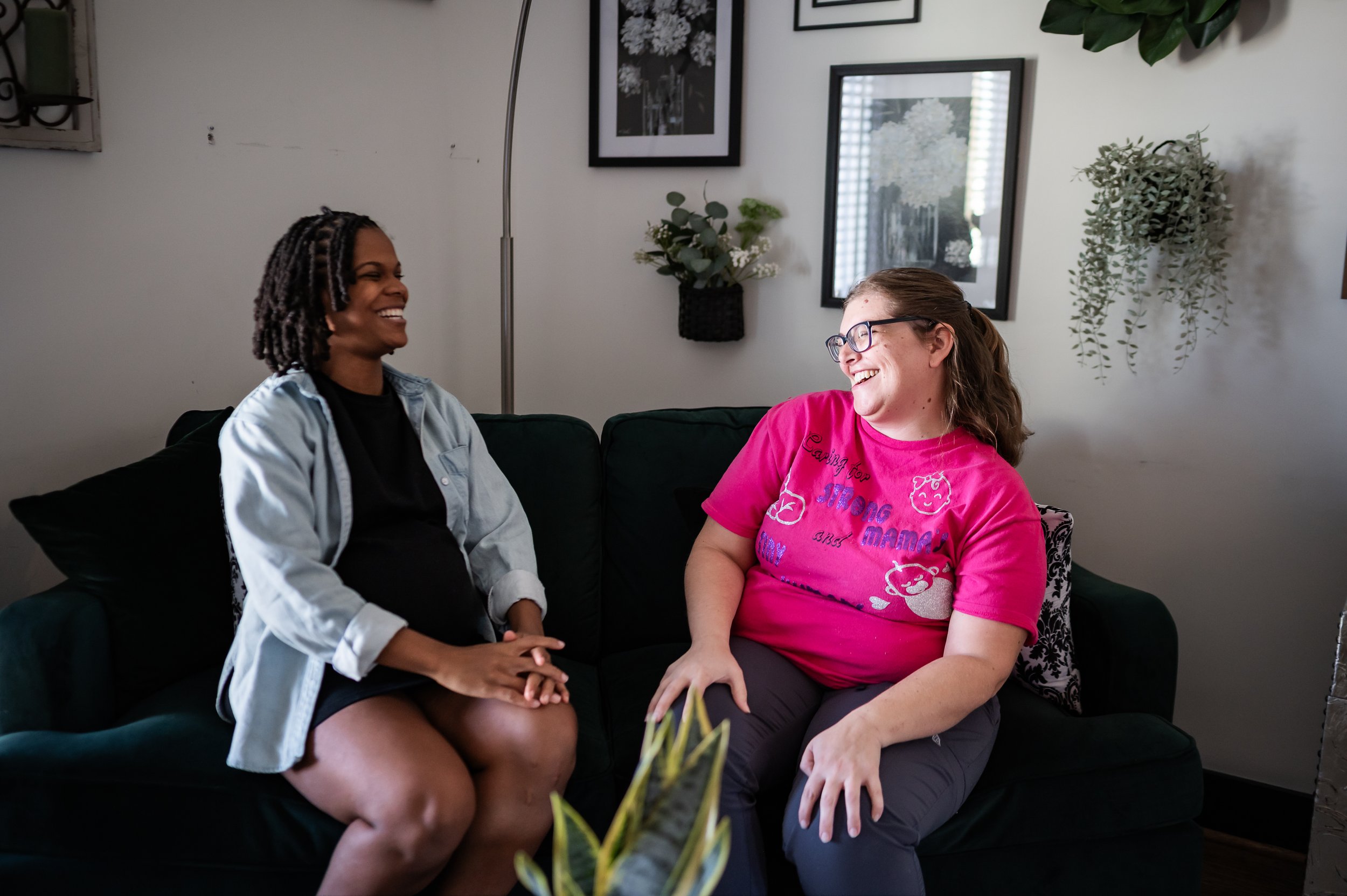 "Doula Melanie Powell sitting on a couch laughing with new mom as they connect and build confidence."